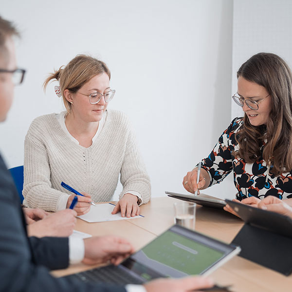 Partnerin schreibt etwas an Tablet und unterhält sich dabei mit anderen Beratern